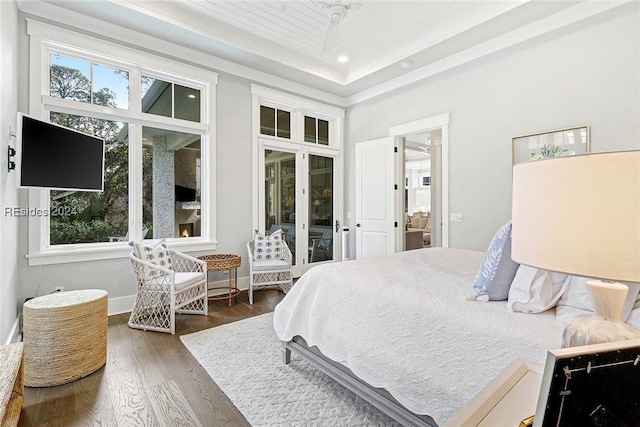 bedroom with a raised ceiling, dark hardwood / wood-style floors, access to outside, and ceiling fan