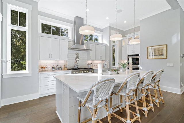 kitchen featuring decorative light fixtures, an island with sink, white cabinets, island exhaust hood, and backsplash