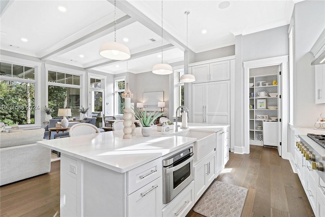 kitchen with hanging light fixtures, appliances with stainless steel finishes, white cabinets, and a center island with sink