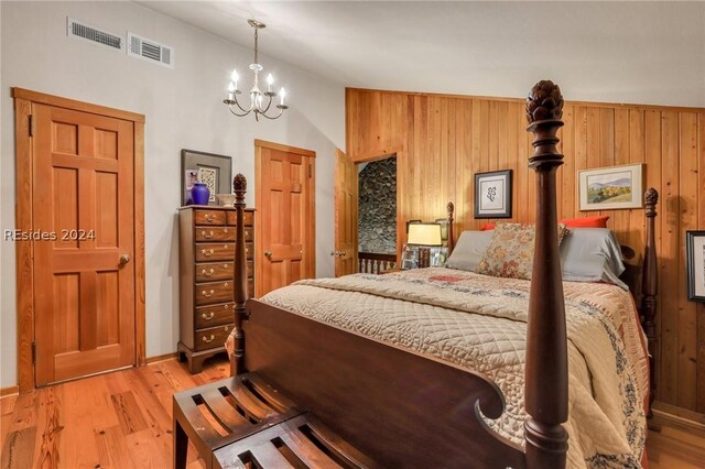 bedroom featuring lofted ceiling, wooden walls, a chandelier, and light hardwood / wood-style floors