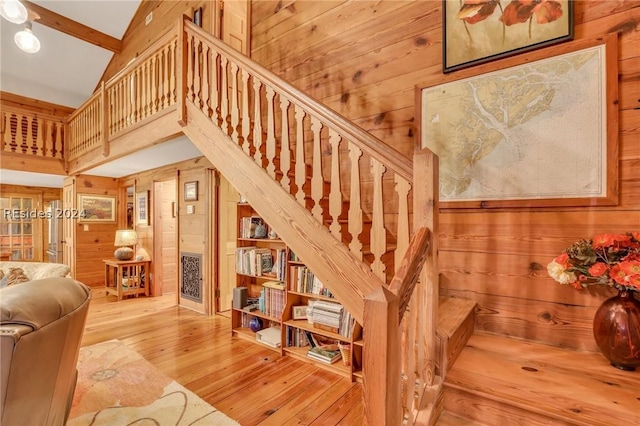 stairway featuring hardwood / wood-style flooring, wooden walls, high vaulted ceiling, and beamed ceiling