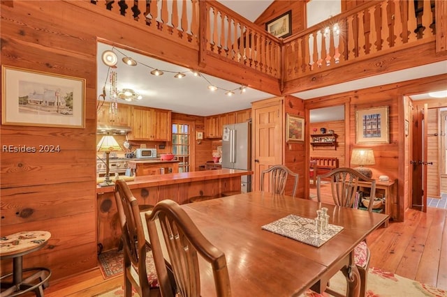 dining area with a towering ceiling, light hardwood / wood-style flooring, and wood walls