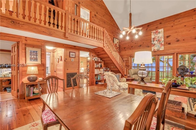 dining area with a notable chandelier, high vaulted ceiling, light hardwood / wood-style floors, and wood walls