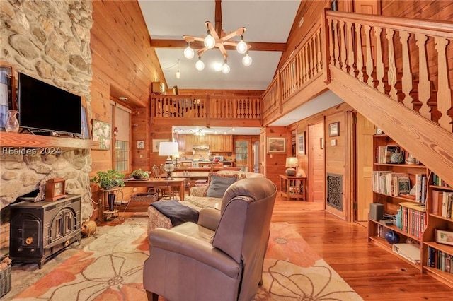 living room with high vaulted ceiling, a wood stove, light wood-type flooring, a notable chandelier, and beam ceiling