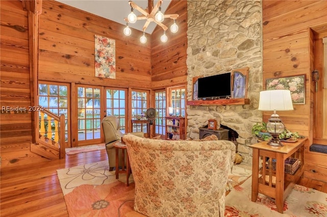 living room with wooden walls, a high ceiling, light hardwood / wood-style floors, french doors, and a wood stove