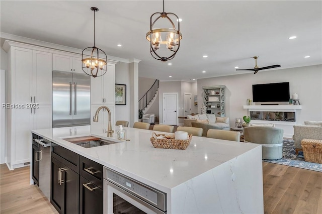 kitchen with sink, hanging light fixtures, built in appliances, light hardwood / wood-style floors, and a center island with sink