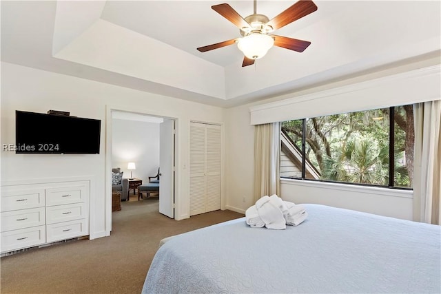 carpeted bedroom with a tray ceiling, a closet, and ceiling fan