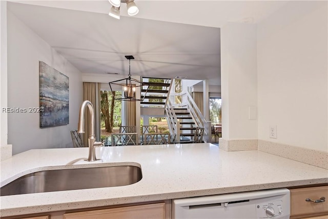 kitchen featuring pendant lighting, sink, an inviting chandelier, white dishwasher, and light stone countertops