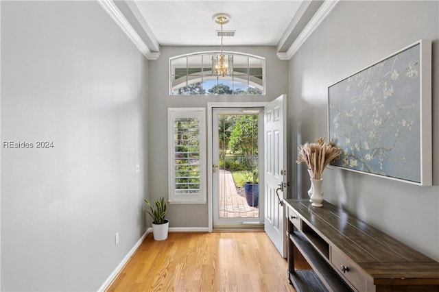 entryway featuring crown molding, a healthy amount of sunlight, a chandelier, and light wood-type flooring