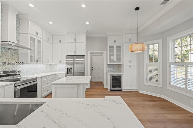 kitchen with wall chimney exhaust hood, white cabinetry, pendant lighting, stainless steel appliances, and beverage cooler