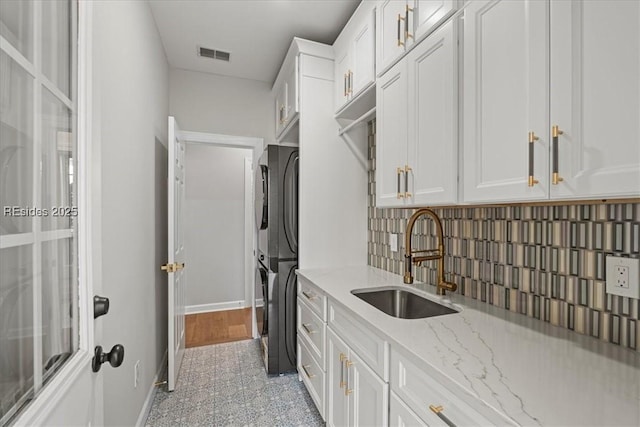 kitchen with sink, light stone counters, refrigerator, white cabinets, and backsplash