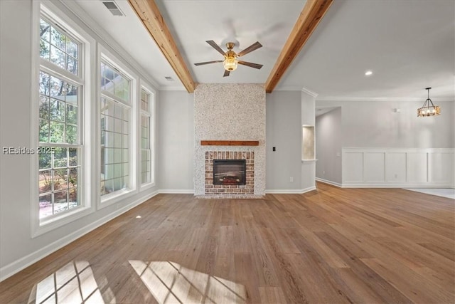 unfurnished living room with ornamental molding, beam ceiling, a brick fireplace, and light hardwood / wood-style flooring