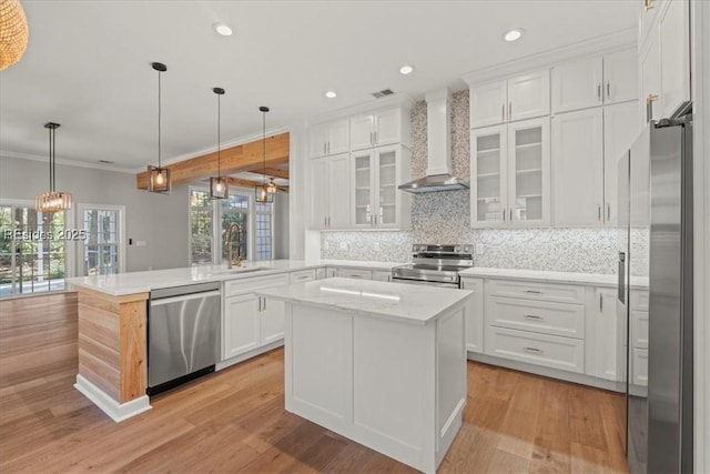 kitchen with white cabinets, a center island, kitchen peninsula, stainless steel appliances, and wall chimney range hood