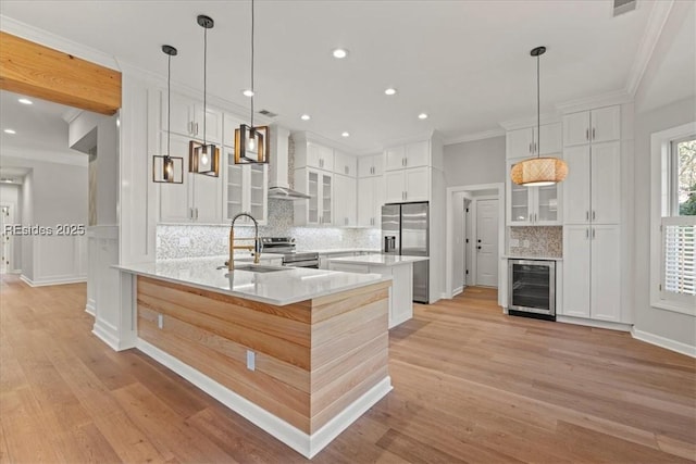 kitchen featuring wall chimney range hood, stainless steel appliances, beverage cooler, and white cabinets