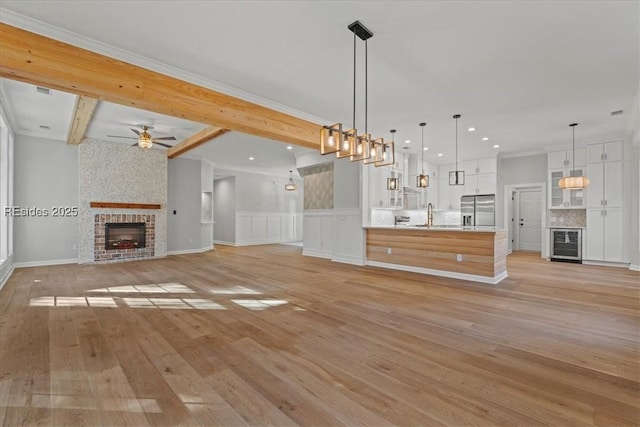 unfurnished living room with beamed ceiling, ornamental molding, beverage cooler, and a fireplace