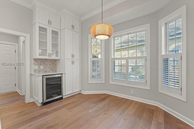 unfurnished dining area with ornamental molding, bar, wine cooler, and light wood-type flooring