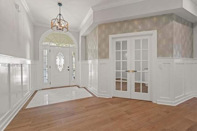 entryway with crown molding, wood-type flooring, a chandelier, and french doors