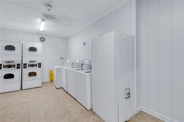 clothes washing area featuring stacked washing maching and dryer, washer and dryer, light tile patterned flooring, and wooden walls