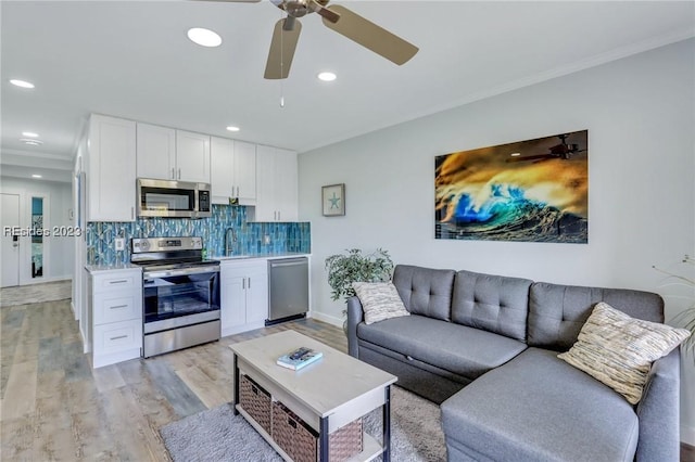 living room featuring ornamental molding, sink, ceiling fan, and light hardwood / wood-style floors