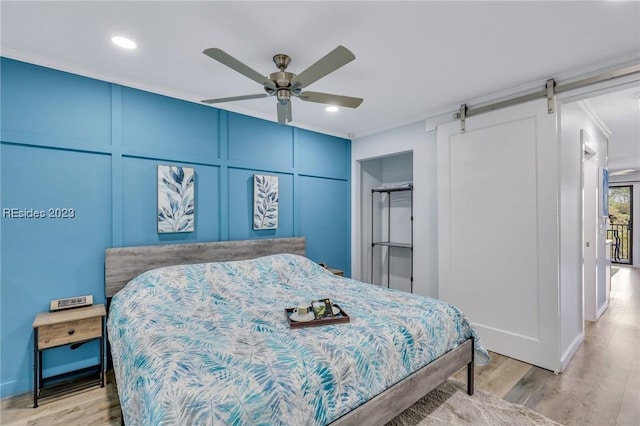 bedroom featuring crown molding, ceiling fan, a barn door, and light wood-type flooring