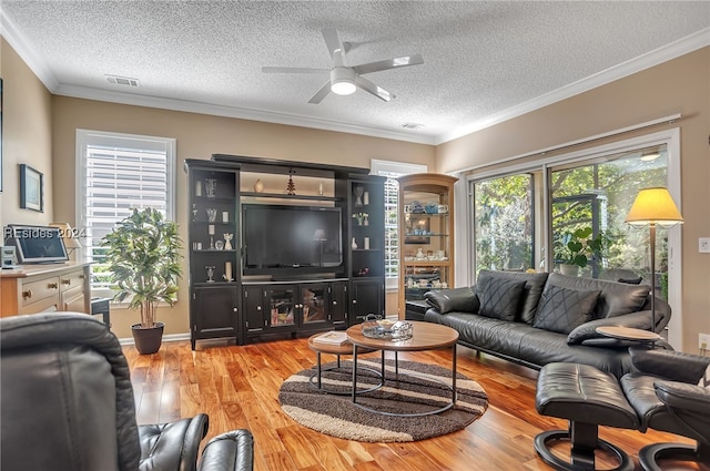 living room with ceiling fan, ornamental molding, light hardwood / wood-style floors, and a textured ceiling