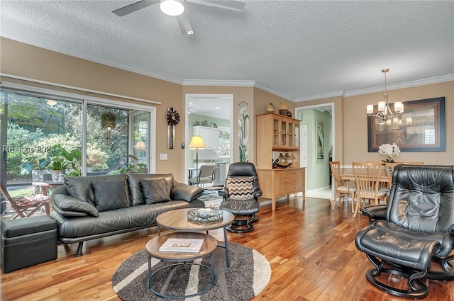 living room with crown molding, ceiling fan with notable chandelier, a textured ceiling, and light wood-type flooring