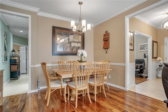 dining space featuring an inviting chandelier, crown molding, a textured ceiling, and light wood-type flooring