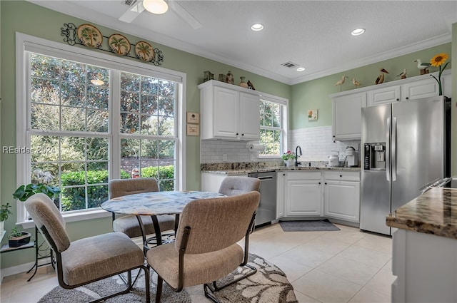 kitchen with plenty of natural light, stainless steel appliances, light stone countertops, white cabinets, and decorative backsplash