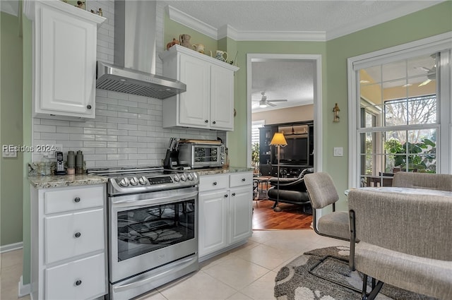 kitchen featuring wall chimney exhaust hood, a textured ceiling, light tile patterned floors, electric range, and white cabinets