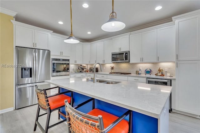 kitchen with appliances with stainless steel finishes, decorative light fixtures, white cabinetry, sink, and a center island with sink