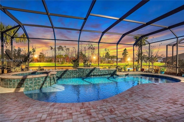 pool at dusk with a lanai, a patio area, and an in ground hot tub