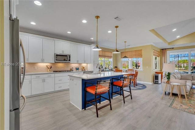 kitchen with a breakfast bar area, appliances with stainless steel finishes, a kitchen island with sink, white cabinets, and decorative light fixtures