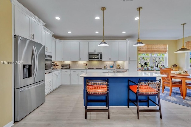 kitchen featuring appliances with stainless steel finishes, pendant lighting, an island with sink, white cabinets, and decorative backsplash