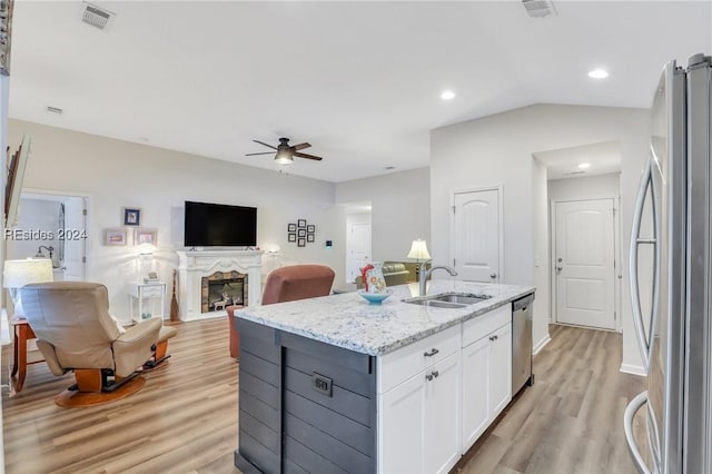 kitchen featuring appliances with stainless steel finishes, white cabinetry, an island with sink, sink, and light stone counters