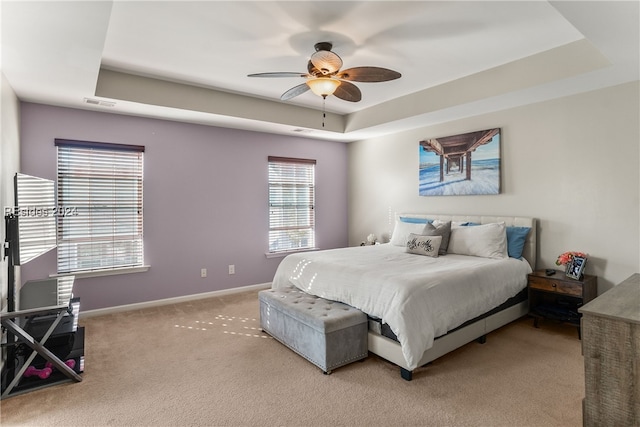 bedroom with ceiling fan, a tray ceiling, and light carpet