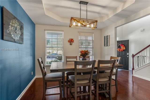 dining space with dark wood-type flooring and a raised ceiling