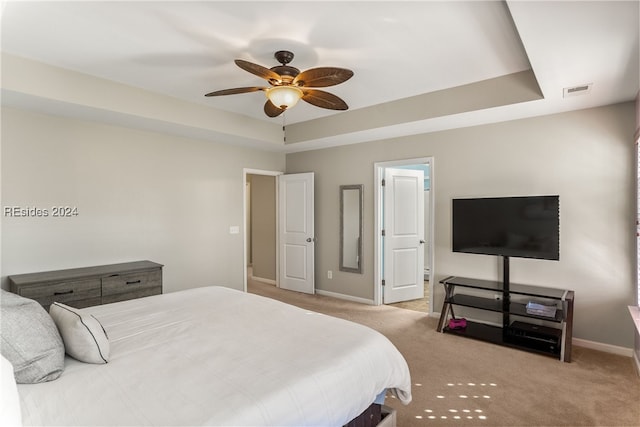 bedroom with a raised ceiling, light carpet, and ceiling fan