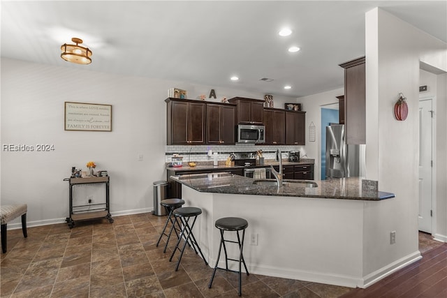 kitchen featuring appliances with stainless steel finishes, a breakfast bar, dark stone countertops, and decorative backsplash