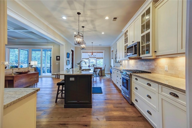 kitchen featuring a kitchen breakfast bar, an island with sink, pendant lighting, stainless steel appliances, and decorative backsplash