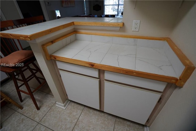 kitchen with tile counters, white cabinets, a kitchen breakfast bar, and kitchen peninsula