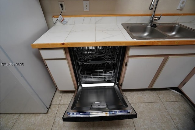 kitchen featuring white cabinetry, dishwashing machine, sink, and light tile patterned floors