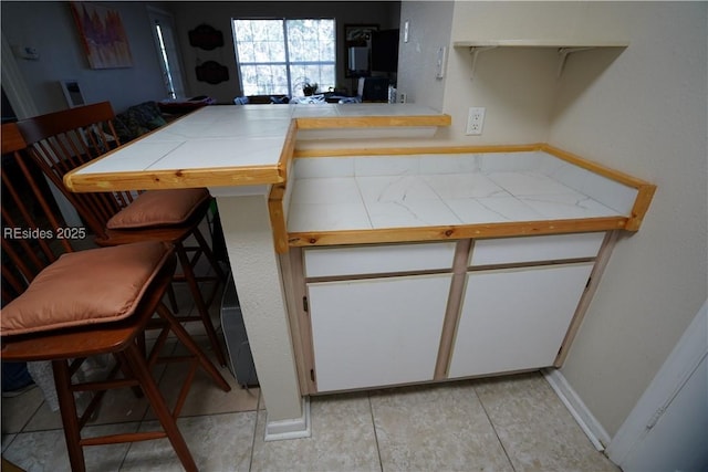 kitchen featuring tile countertops, a breakfast bar area, kitchen peninsula, and white cabinets