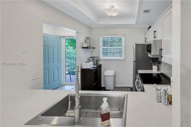 kitchen with white cabinetry, a tray ceiling, stainless steel range oven, and crown molding