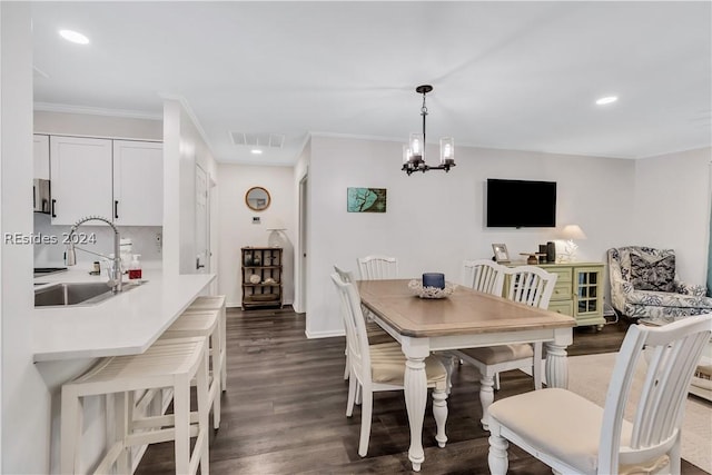 dining space with sink, a notable chandelier, ornamental molding, and dark hardwood / wood-style floors