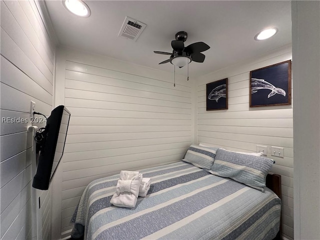 bedroom with ceiling fan and wood walls