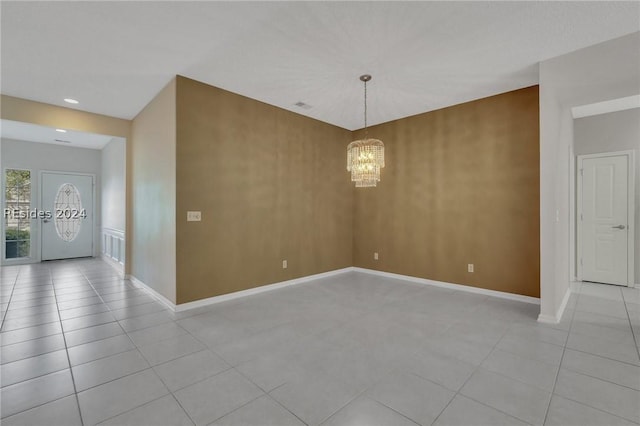 empty room with light tile patterned floors and a chandelier