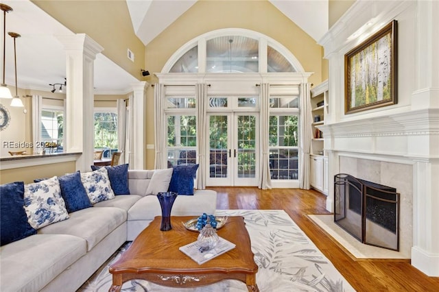 living room featuring decorative columns, vaulted ceiling, a fireplace, and light hardwood / wood-style floors