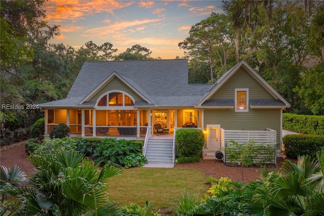 back house at dusk featuring a porch and a lawn