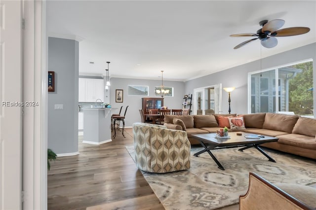 living room featuring ceiling fan with notable chandelier, ornamental molding, sink, and hardwood / wood-style floors