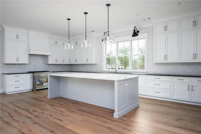 kitchen featuring premium range hood, white cabinetry, high end range, decorative light fixtures, and light hardwood / wood-style floors